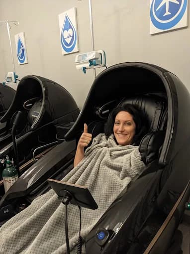 A smiling client giving a thumbs-up while relaxing in a heated massage chair at Prime IV Hydration Mesa, AZ